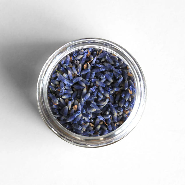 Small glass container filled with dried lavender flowers on a white background
