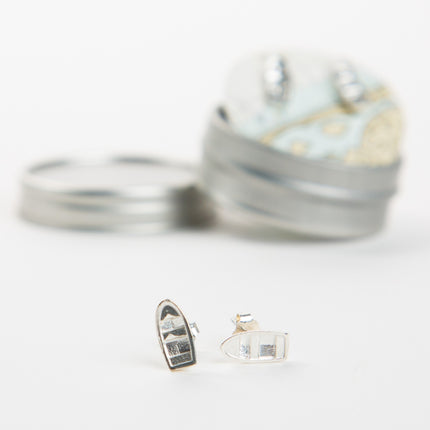 Silver earrings resembling boats on a white background