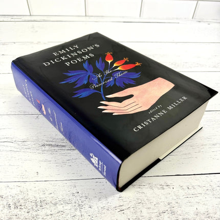 Book titled 'Emily Dickinson's Poems' with a cover illustration of a hand holding flowers on a white wooden surface.