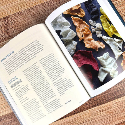 Open book with text and a colorful display of puffed snacks on a wooden surface