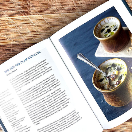 Open cookbook showing a page with New England Clam Chowder recipe and a photograph of the dish.