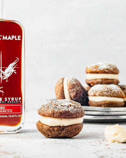 a bottle of festivus infused maple syrup on a countertop next to some gingerbread whoopie pies, highlighting the syrup's potential for use as a baking/flavoring ingredient