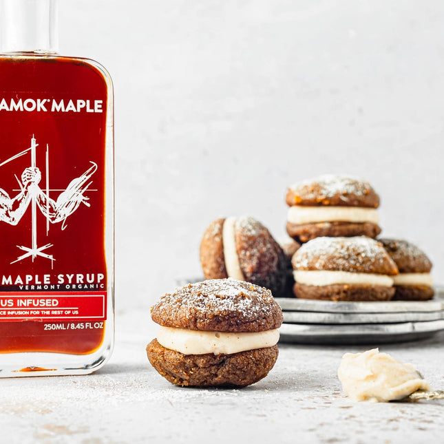 a bottle of festivus infused maple syrup on a countertop next to some gingerbread whoopie pies, highlighting the syrup's potential for use as a baking/flavoring ingredient