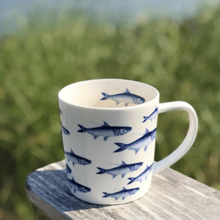White mug with blue fish pattern on a wooden surface with a grassy background