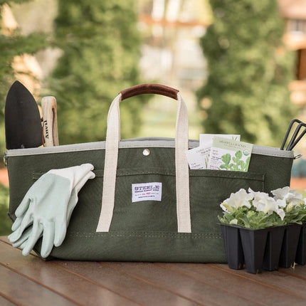 the garden tote loaded with tools, gloves, and seed packets sitting on a table alongside a pack of white flowers