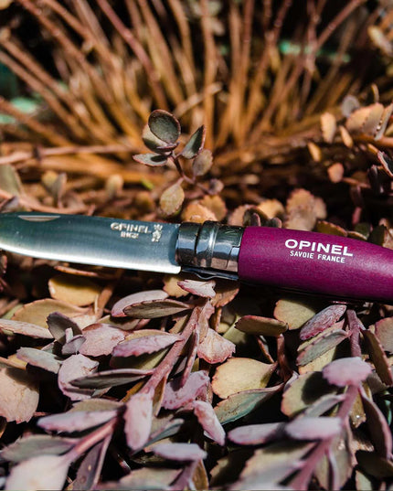 a close up of the No. 08 Garden Knife with purple handle resting on a bed of garden cuttings