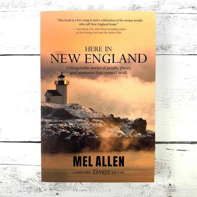 Book cover of 'Here in New England' by Mel Allen with a lighthouse on a rocky shore.