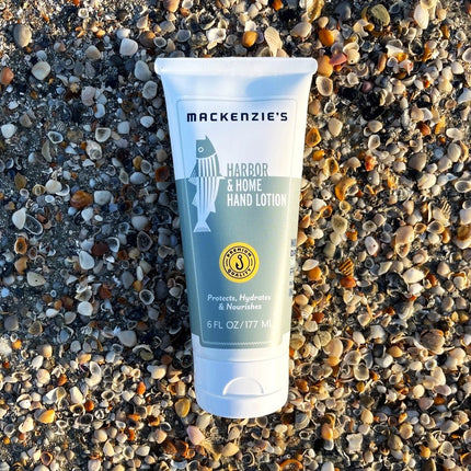 a bottle of the Harbor and Home Hand lotion with white and sea green label on a pebbled beach