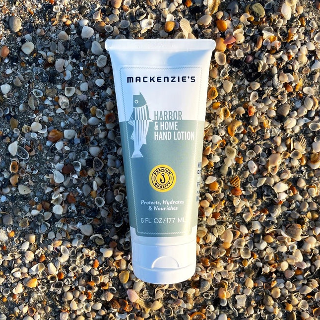 a bottle of the Harbor and Home Hand lotion with white and sea green label on a pebbled beach