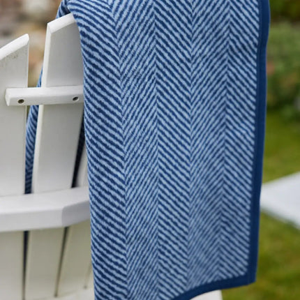 The folded Harborview Herringbone Navy Blanket draped over a white Adirondack chair