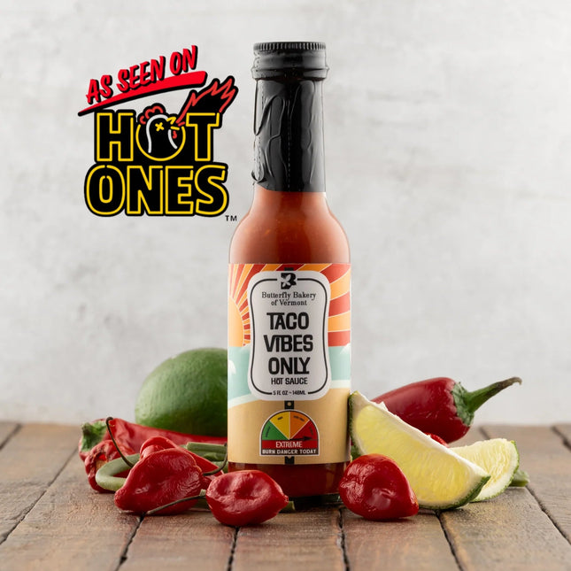Bottle of 'Taco Vibes Only' hot sauce with peppers and lime on a wooden surface, featuring 'Hot Ones' branding.