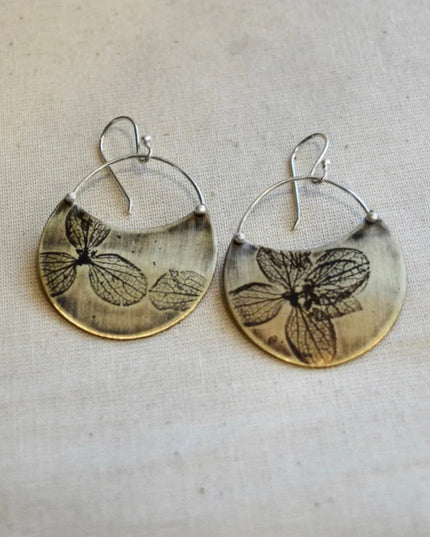 Pair of earrings with pressed hydrangea petal designs on a textured fabric background