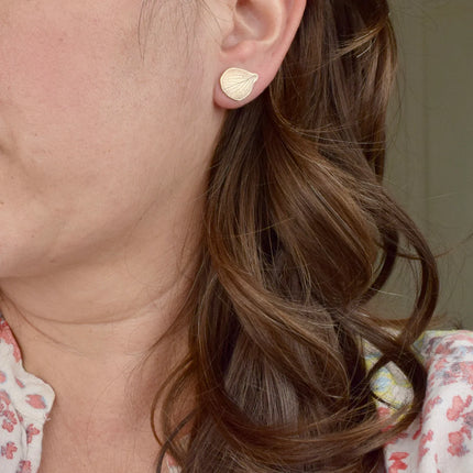 Close-up of a person wearing brass hydrangea petal shaped earrings with a blurred background.