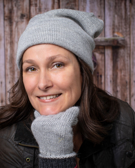 a smiling woman wears the silver iditarod hat and matching gloves posing casually with her chin resting on her gloved fist