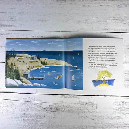 Open book with a scenic illustration of a coastal village and text on a wooden surface