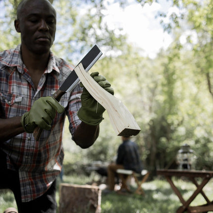a man at a lush forest campsite splitting firewood with his japanese nata hatchet