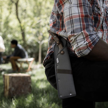 close up of the japanese nata hatchet in its sheath on attached to a man's belt as he stands at a lush forest campsite