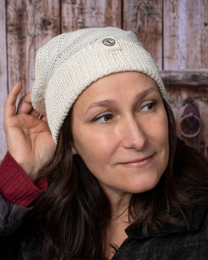 a fair skinned, brunette female model wearing the Cream beanie with her hand at the back of her head as if adjusting or styling it