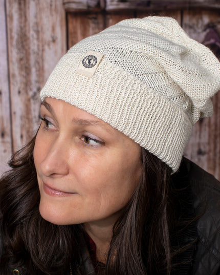 a fair skinned, brunette female model wearing the Cream beanie - she is smiling softly and posed in front of a rustic barn door