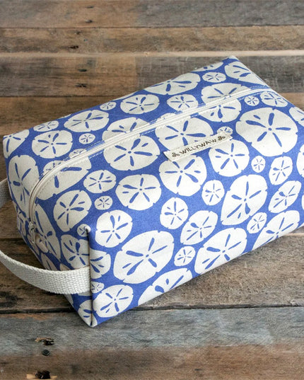 Blue toiletry bag with white sand dollar pattern on a wooden surface