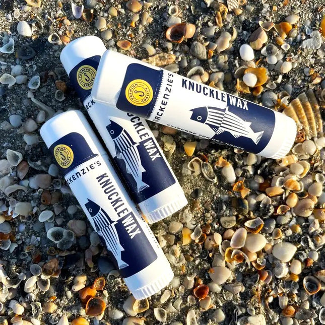 a trio of Knuckle Wax sticks on a pebbled beach