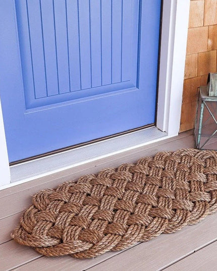 a side angle view of a large manila rope doormat with an intricate hand woven pattern on a doorstep in front of a sky blue door