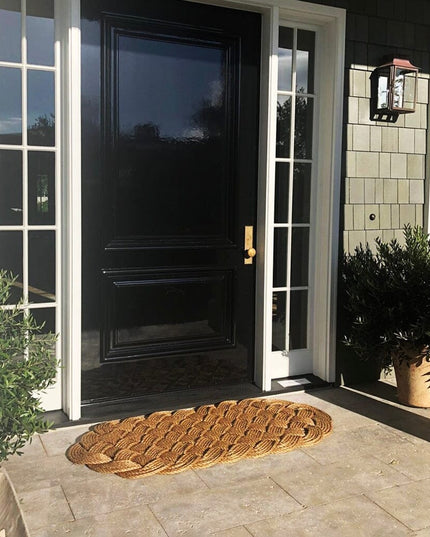 wide shot of a a large manila rope doormat with an intricate hand woven pattern on a doorstep in front of a navy blue door