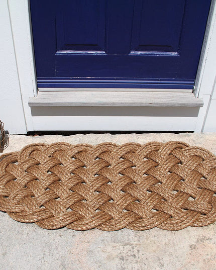a large manila rope doormat with an intricate hand woven pattern on a doorstep in front of a navy blue door