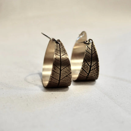 Pair of bronze hoop earrings with pressed leaf patterns on a light background