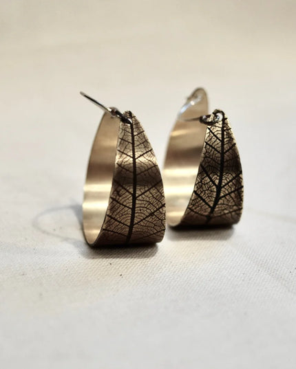 Pair of bronze hoop earrings with pressed leaf patterns on a light background