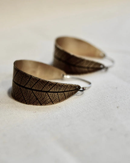 Pair of leaf-patterned earrings on a light fabric background