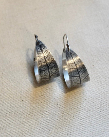 Silver leaf-shaped earrings on a beige fabric background