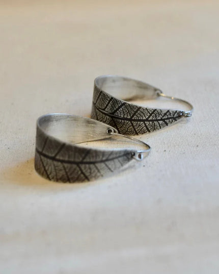 Silver leaf-shaped earrings on a light fabric background