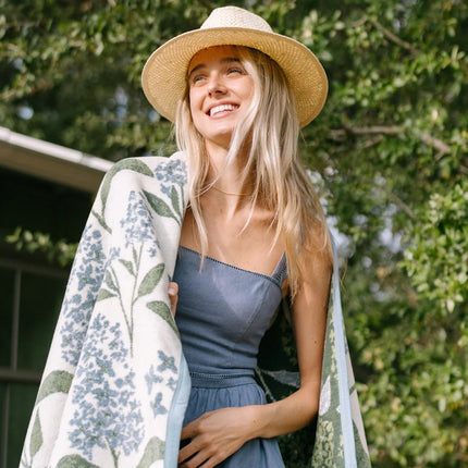 Woman wearing a straw hat with the lilacs blanket wrapped around her shoulders outdoors