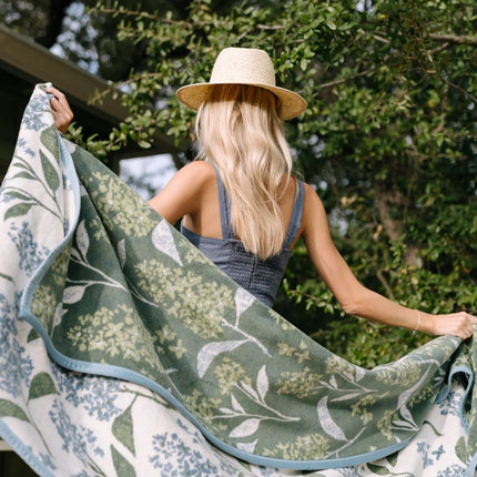 Woman holding a green floral lilac-patterned blanket outdoors