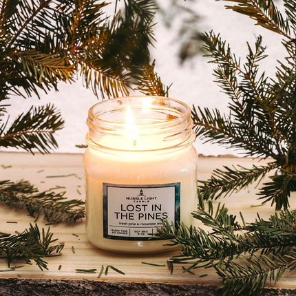 Candle in a jar labeled 'Lost in the Pines' surrounded by pine branches.