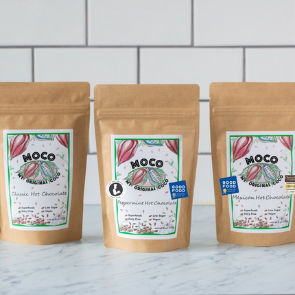 a trio of hot cocoa packages against a white tile background