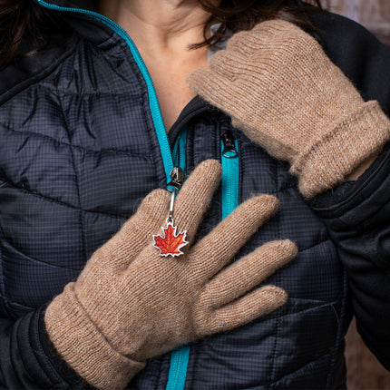 a model wearing a black jacket and camel colored gloves lightly grips the maple leaf zipper pull on her jacket