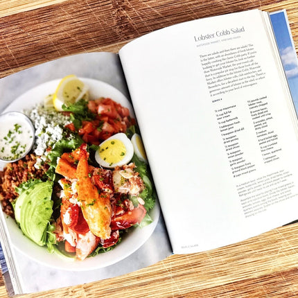 Lobster Cobb Salad on a plate with a recipe book open to a page about the dish.
