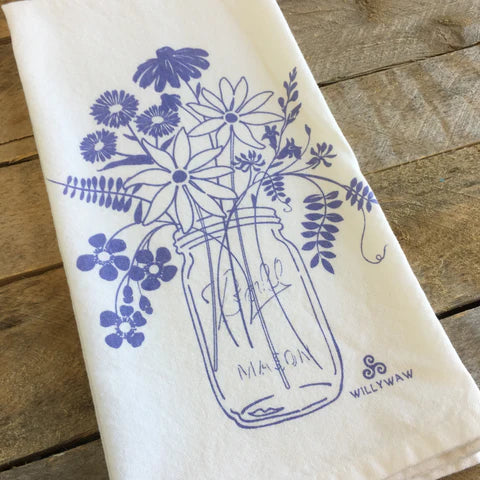 White towel with blue floral design of a mason jar and flowers on a wooden surface