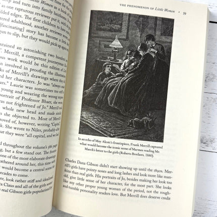 Open book with text and an illustration of a scene from 'Little Women' on a wooden surface.