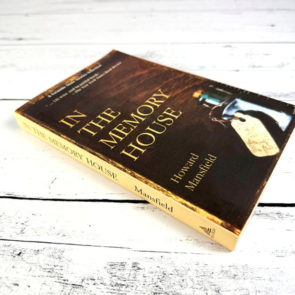the book, In the Memory House, on a white wood surface shown at an angle revealing the book's spine
