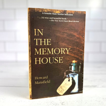 an upright copy of the book, In the Memory House, on a white wood surface with white tiled background