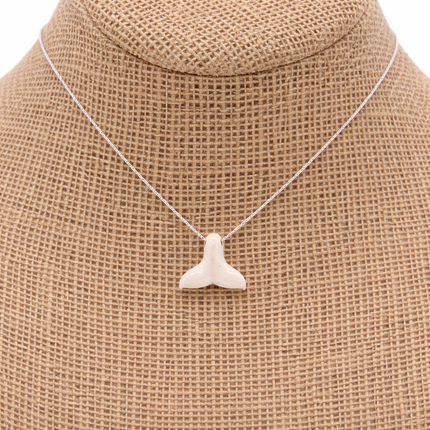 a whale tail pendant on a silver chain on a natural color jewelry bust