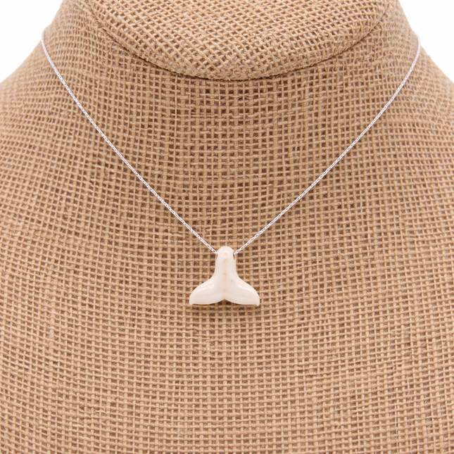 a whale tail pendant on a silver chain on a natural color jewelry bust