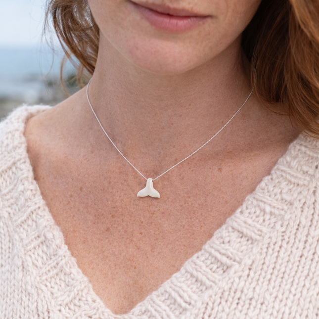Woman wearing a necklace with a whale tail pendant against a blurred natural background