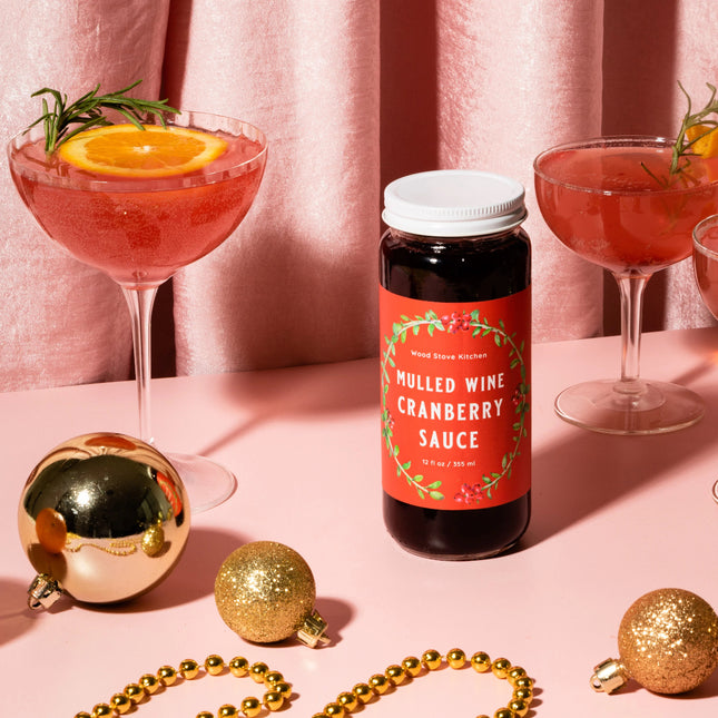 Mulled wine cranberry sauce bottle with cocktails and Christmas ornaments on a pink background