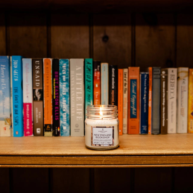 a bookshelf filled with books and a New England Bookshop candle burning on the shelf