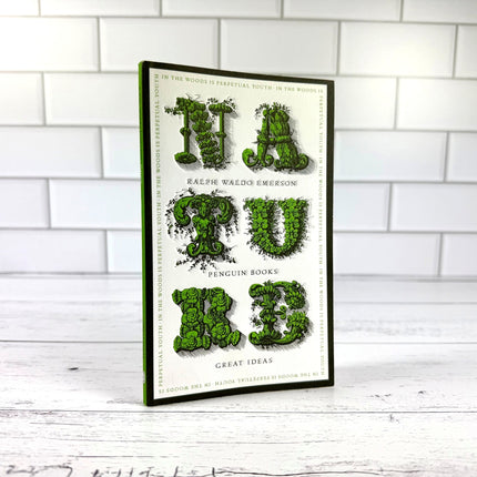 book titled 'NATURE' with text made of leaves on a white brick wall background
