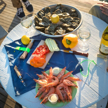 the nomad cooking kit amongst a spread of oysters and shrimp on a dockside table